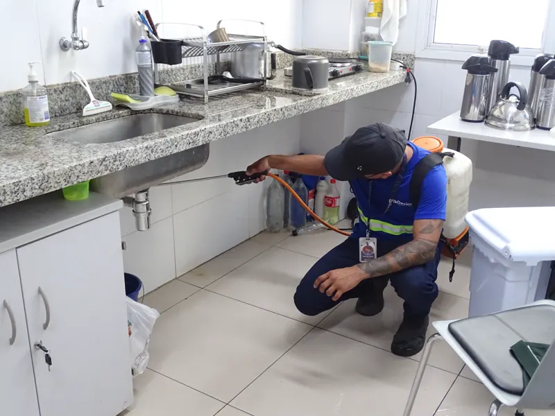 Técnico da Desinsect com EPI fazendo aplicação sob a pia da cozinha